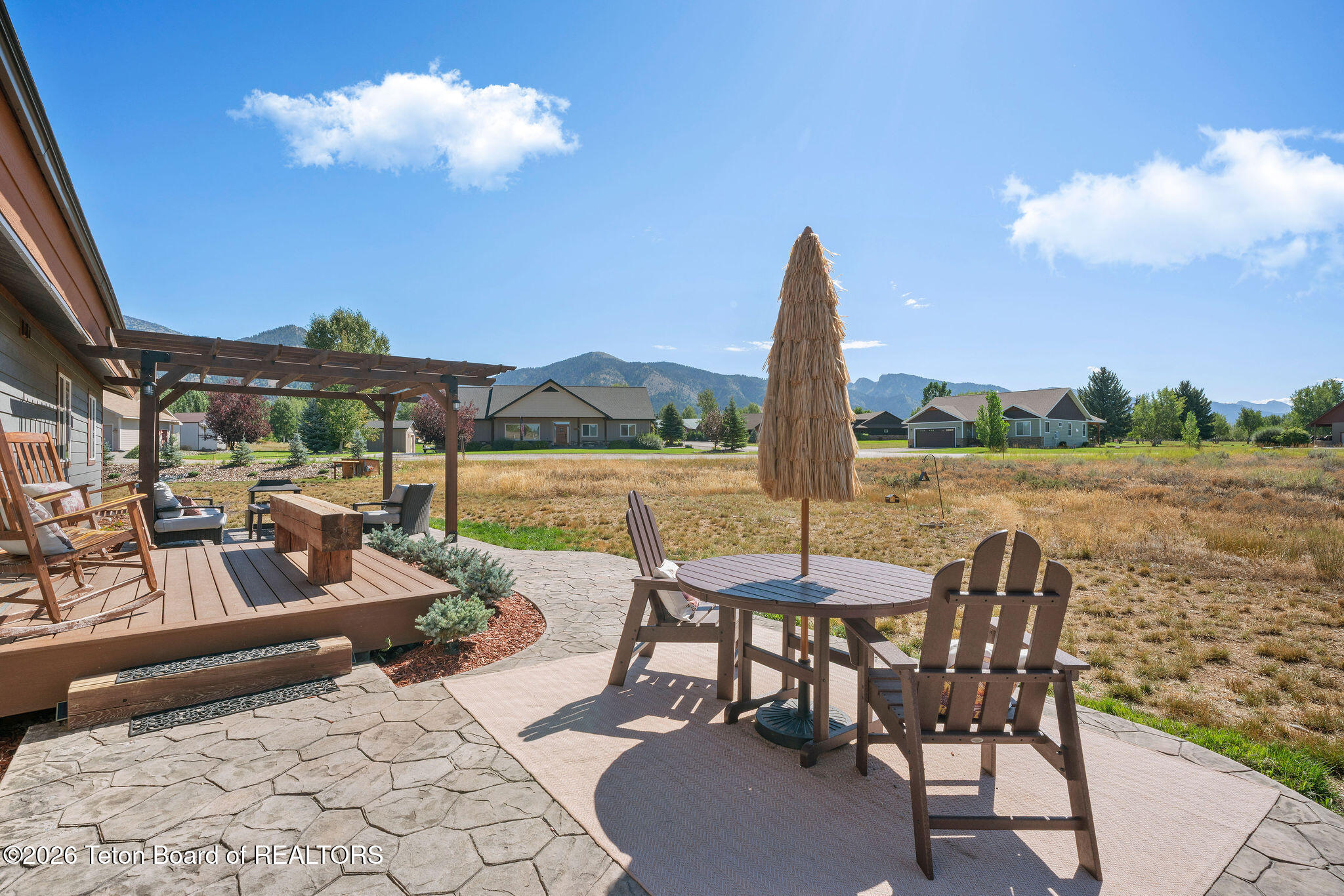Furnished stone patio with a thatched umbrella, Adirondack chairs, and mountain views.