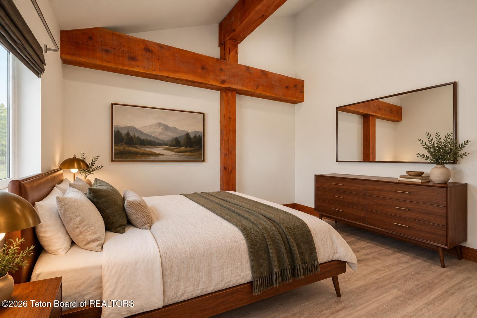 Bedroom with exposed timber beams, a white bed, and a wooden dresser beneath a large mirror.