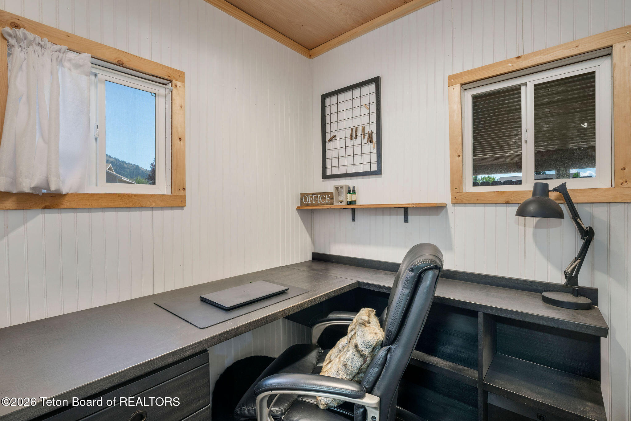 Home office with an L-shaped desk, leather chair, and two wood-trimmed windows.