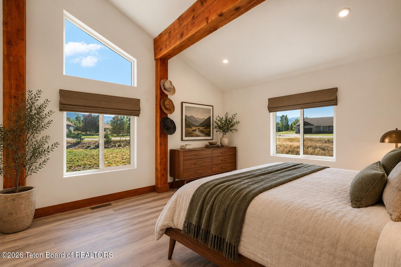 Bedroom with exposed wood beams, a large bed, and two windows overlooking the neighborhood.