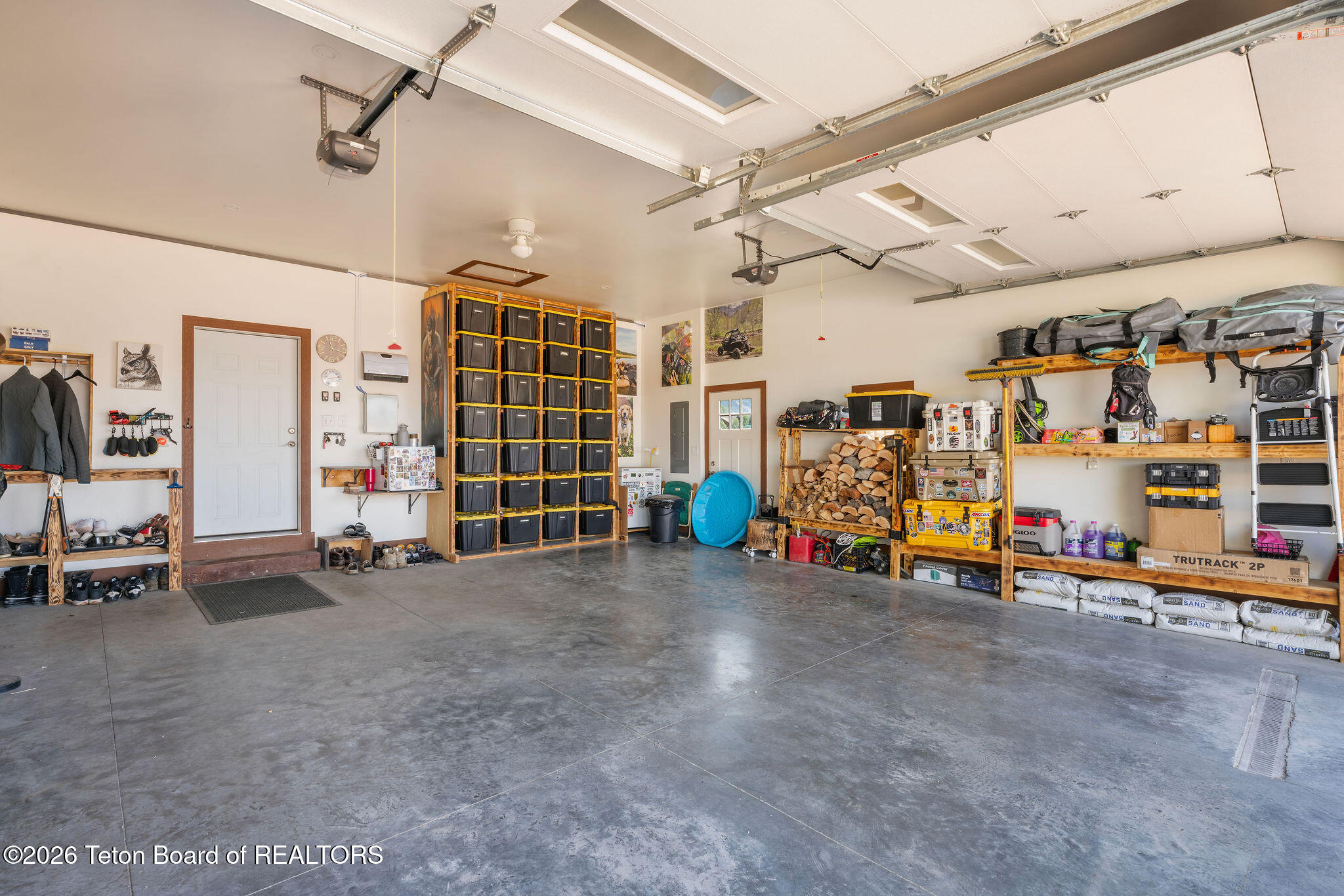 Organized garage with storage-bin shelving, stacked firewood, and a polished concrete floor.