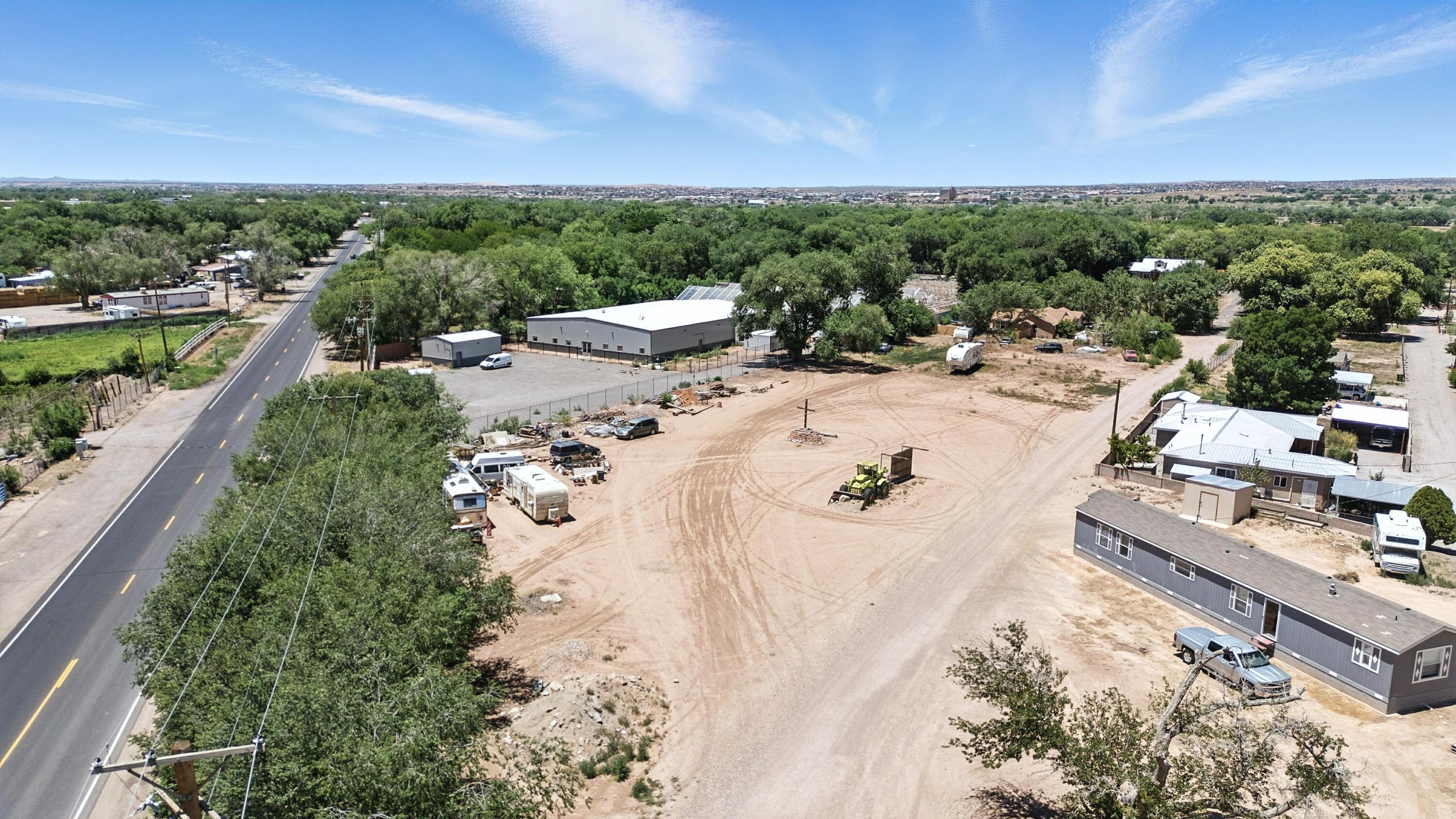 Aerial view of a sandy property with scattered buildings, trailers, and a solar-paneled warehouse beside a road.