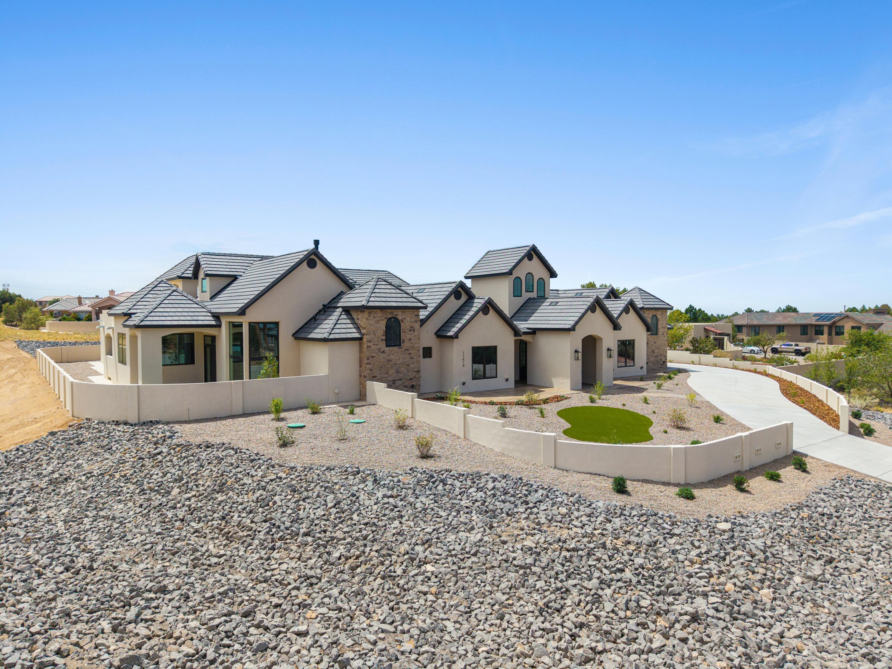 Large stucco and stone home with tiled roofs, enclosed gravel landscaping, and a curved driveway.
