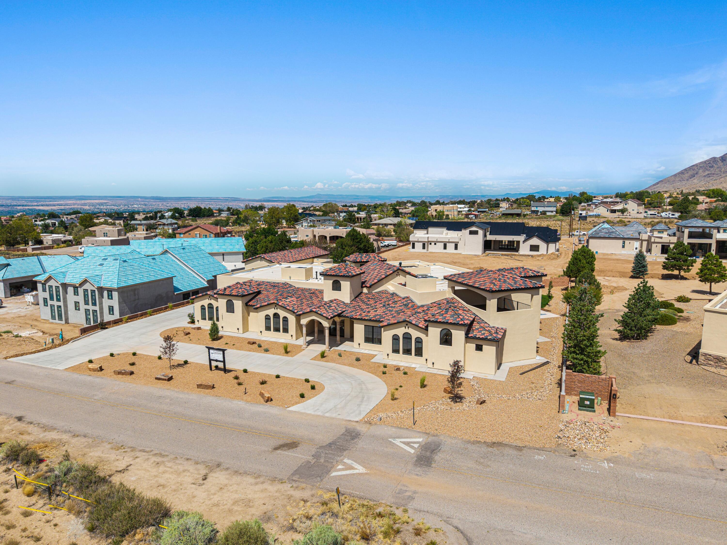 Aerial view of southwestern homes with tile roofs in a desert neighborhood beneath distant mountains.