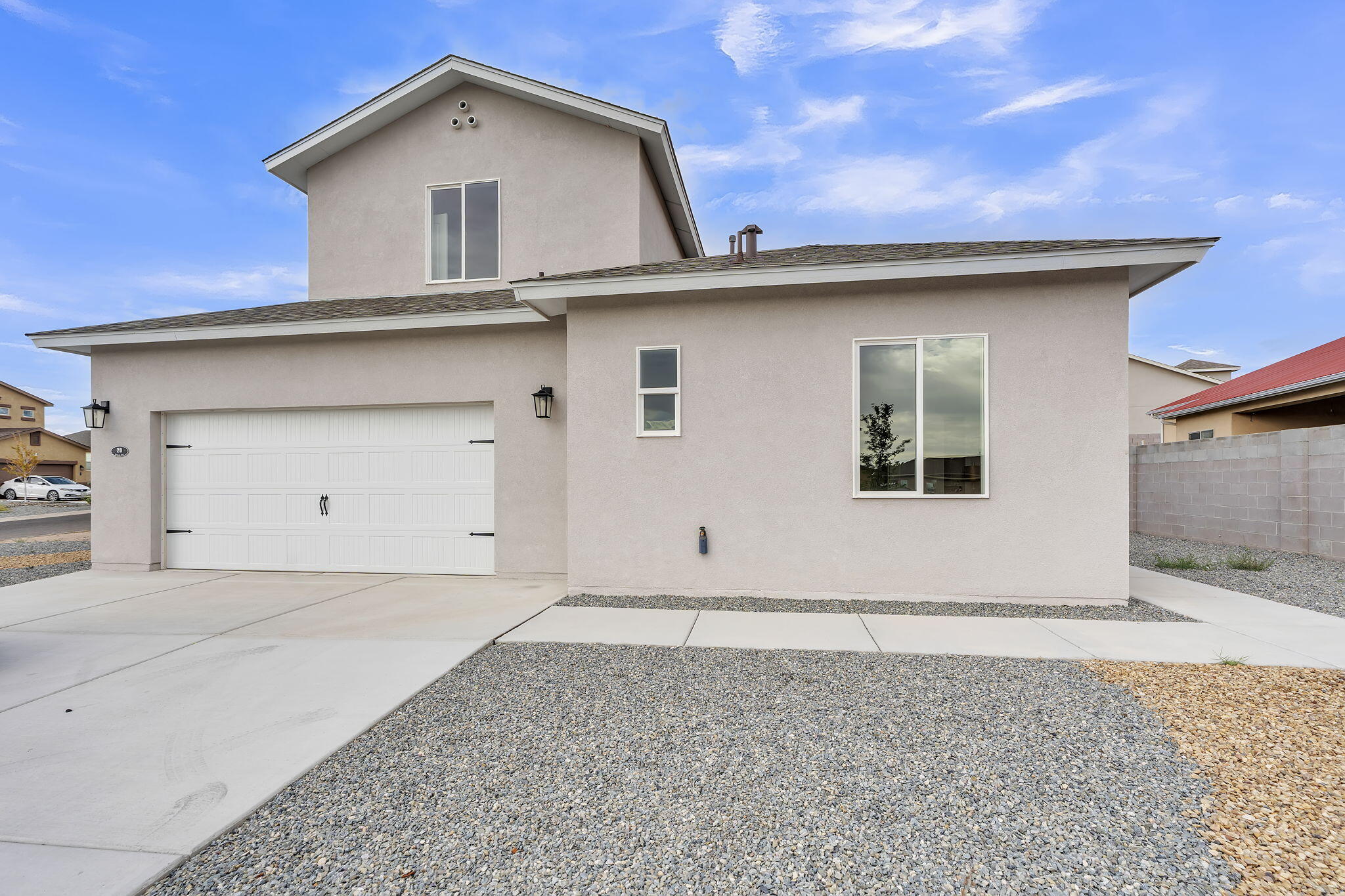 Two-story stucco home with a white double garage, wide driveway, and gravel landscaping.