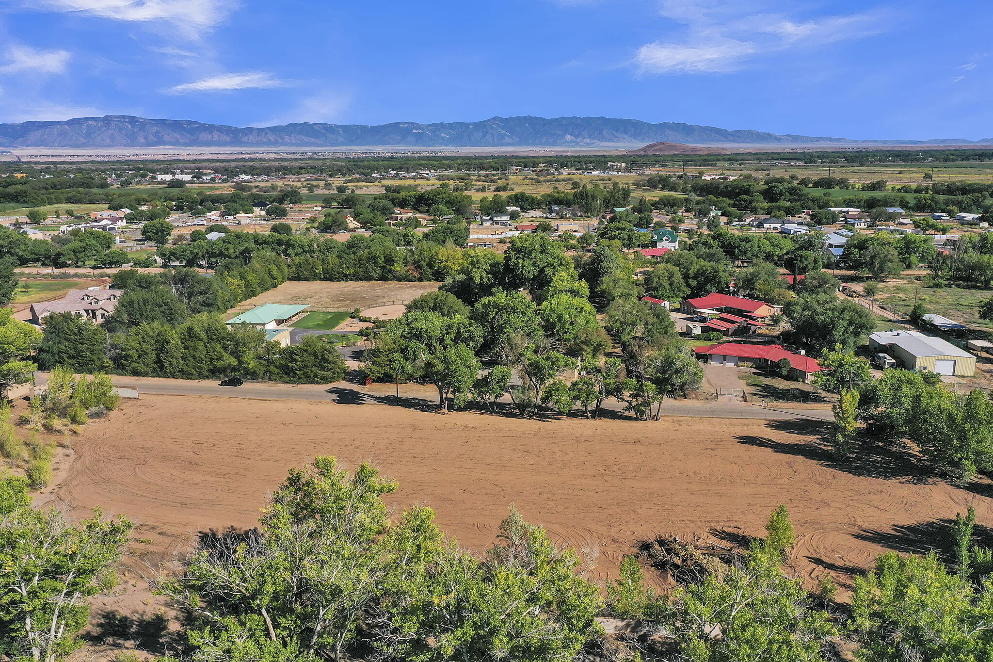 Aerial view of a graded lot bordered by trees, with nearby homes and mountains on the horizon.