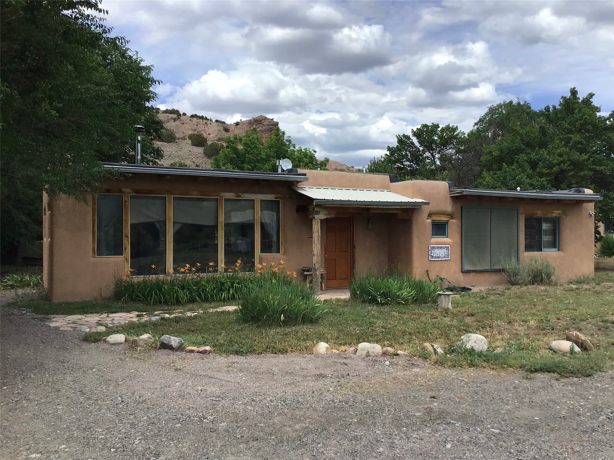 Single-story adobe-style home with large windows, a covered entrance, and rocky hills behind it.