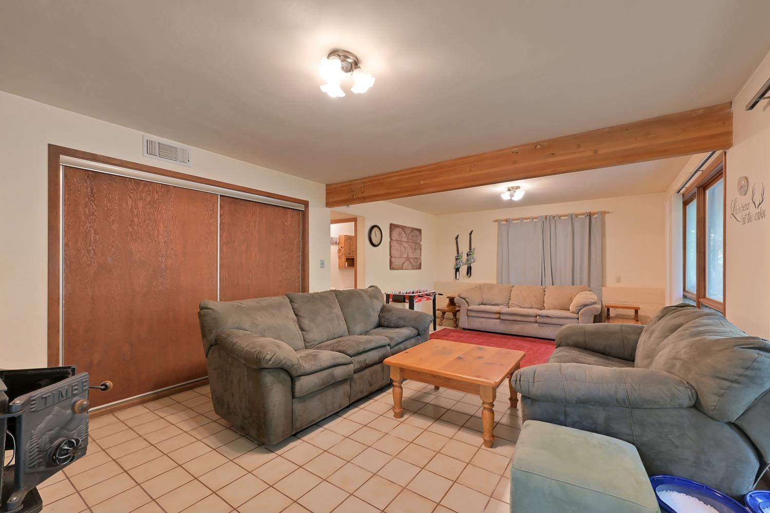 Living room with gray sofas, a tiled floor, exposed wood beam, and wood-burning stove.