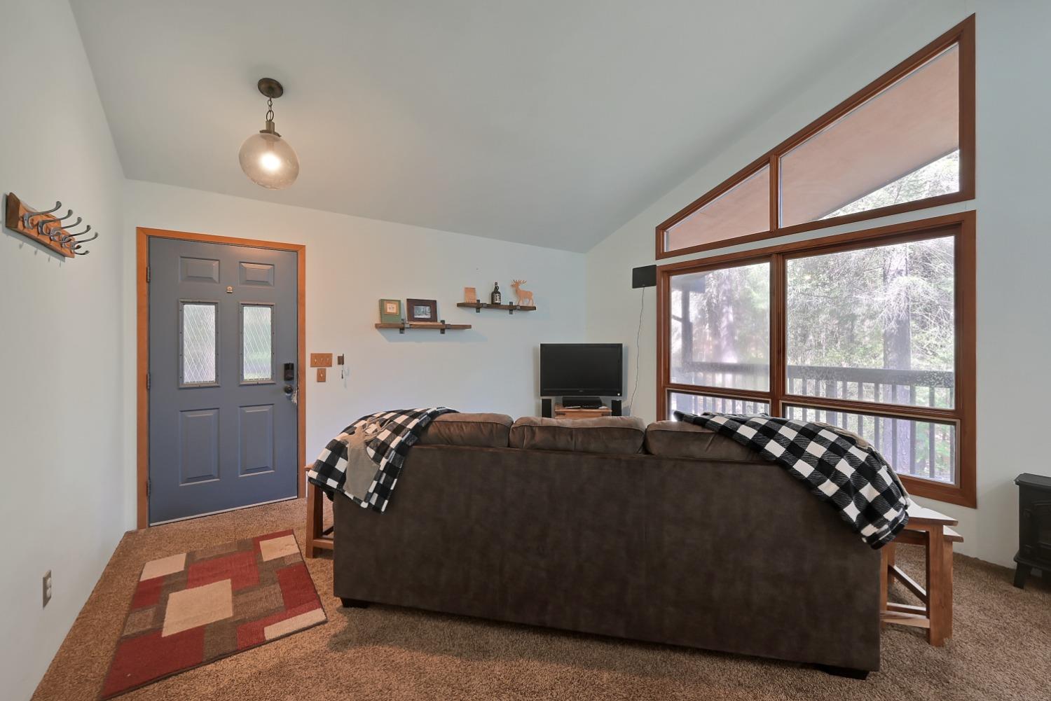 Living room with a vaulted ceiling, large windows overlooking trees, and a dark sofa.
