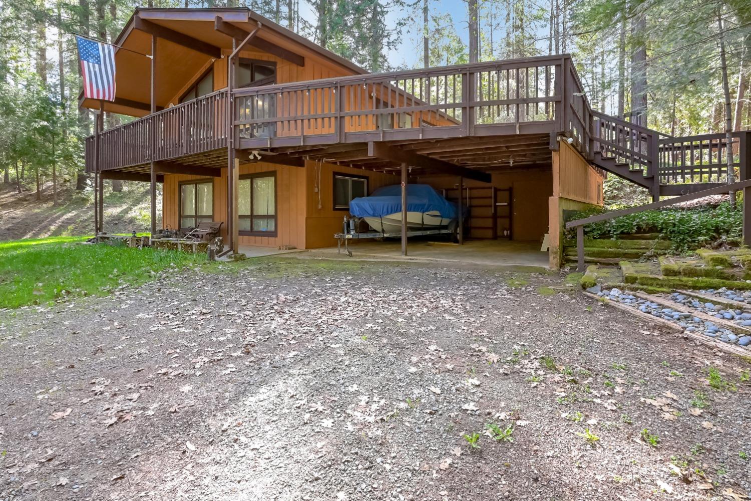 Wood-sided house with a large elevated deck, exterior stairs, and a boat sheltered beneath it.