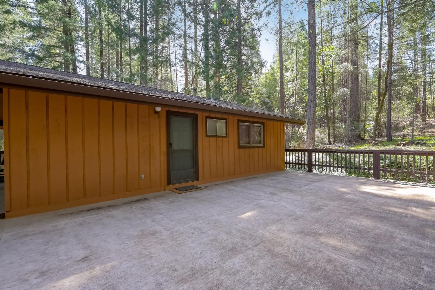Ochre-sided home beside a broad concrete patio, surrounded by tall trees.