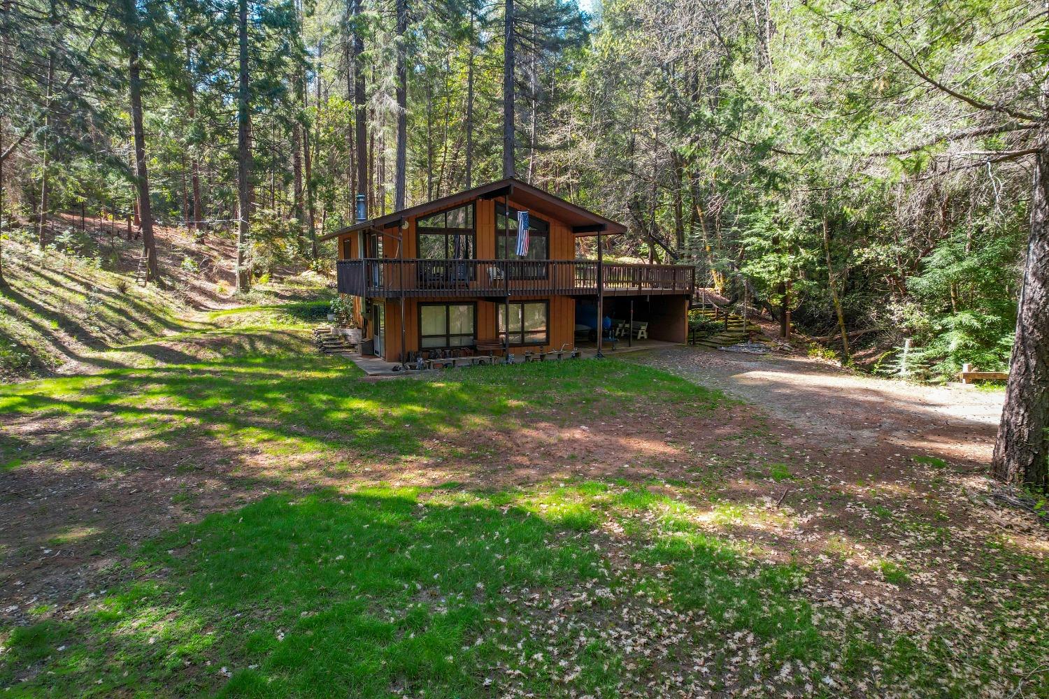 Brown two-story home with a broad deck and covered carport in a wooded clearing.