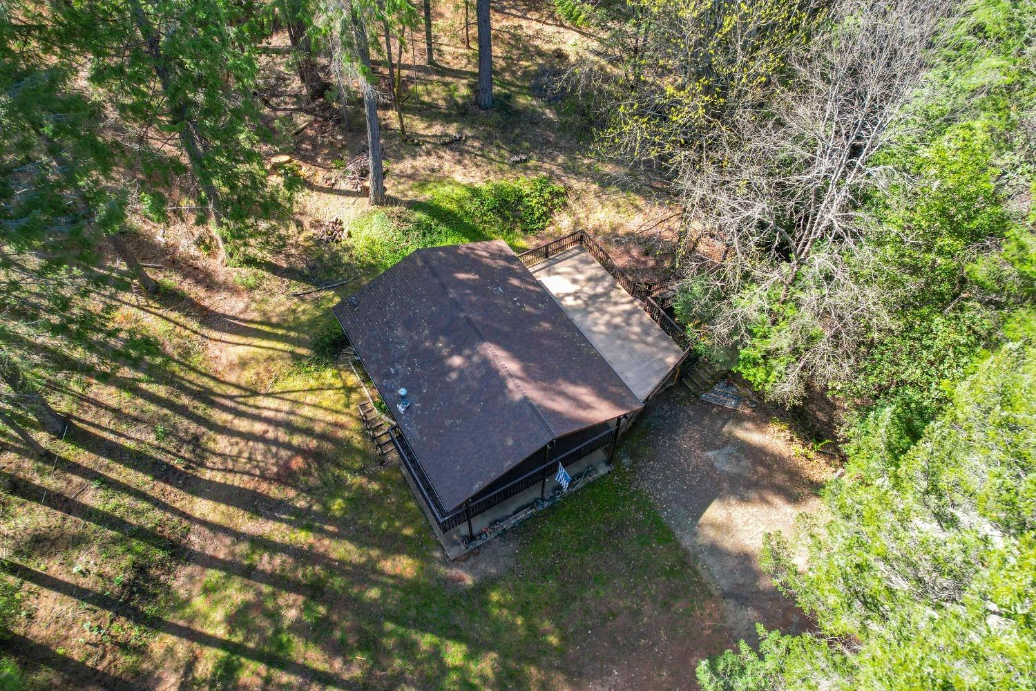 Aerial view of a wooded property with a dark-roofed house and adjoining deck.