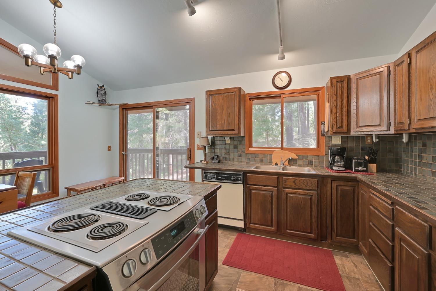 Kitchen with dark wood cabinets, tiled counters, an electric range, and windows overlooking trees.