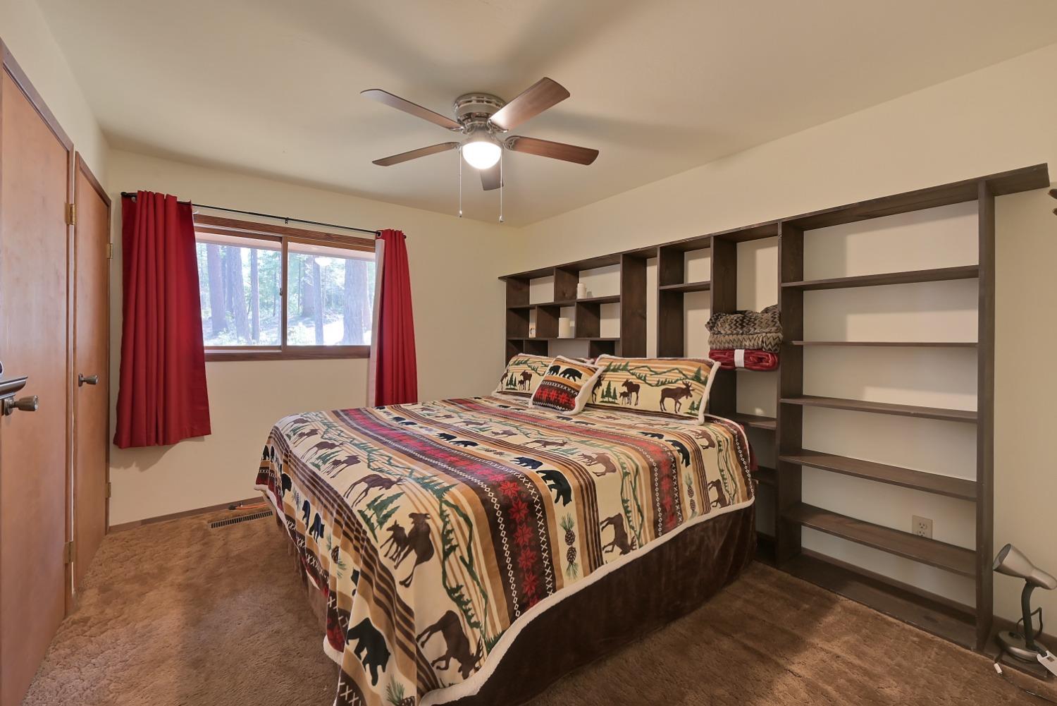 Bedroom with a patterned bedspread, dark built-in shelving, and red curtains.