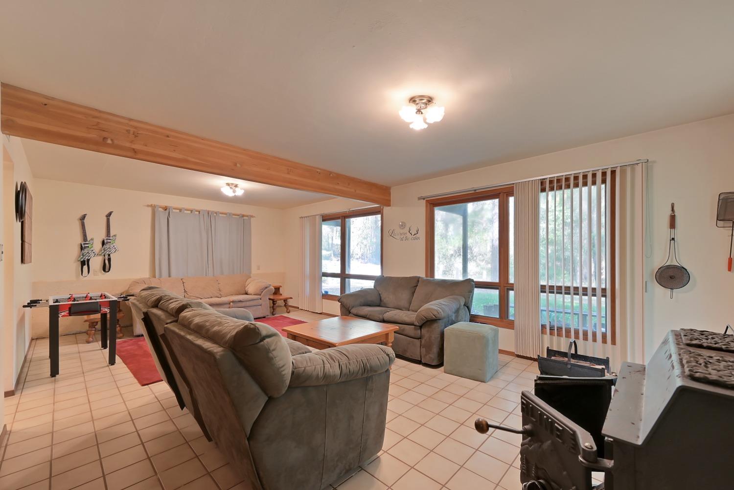 Living room with sectional seating, an exposed wood beam, large windows, and a wood-burning stove.