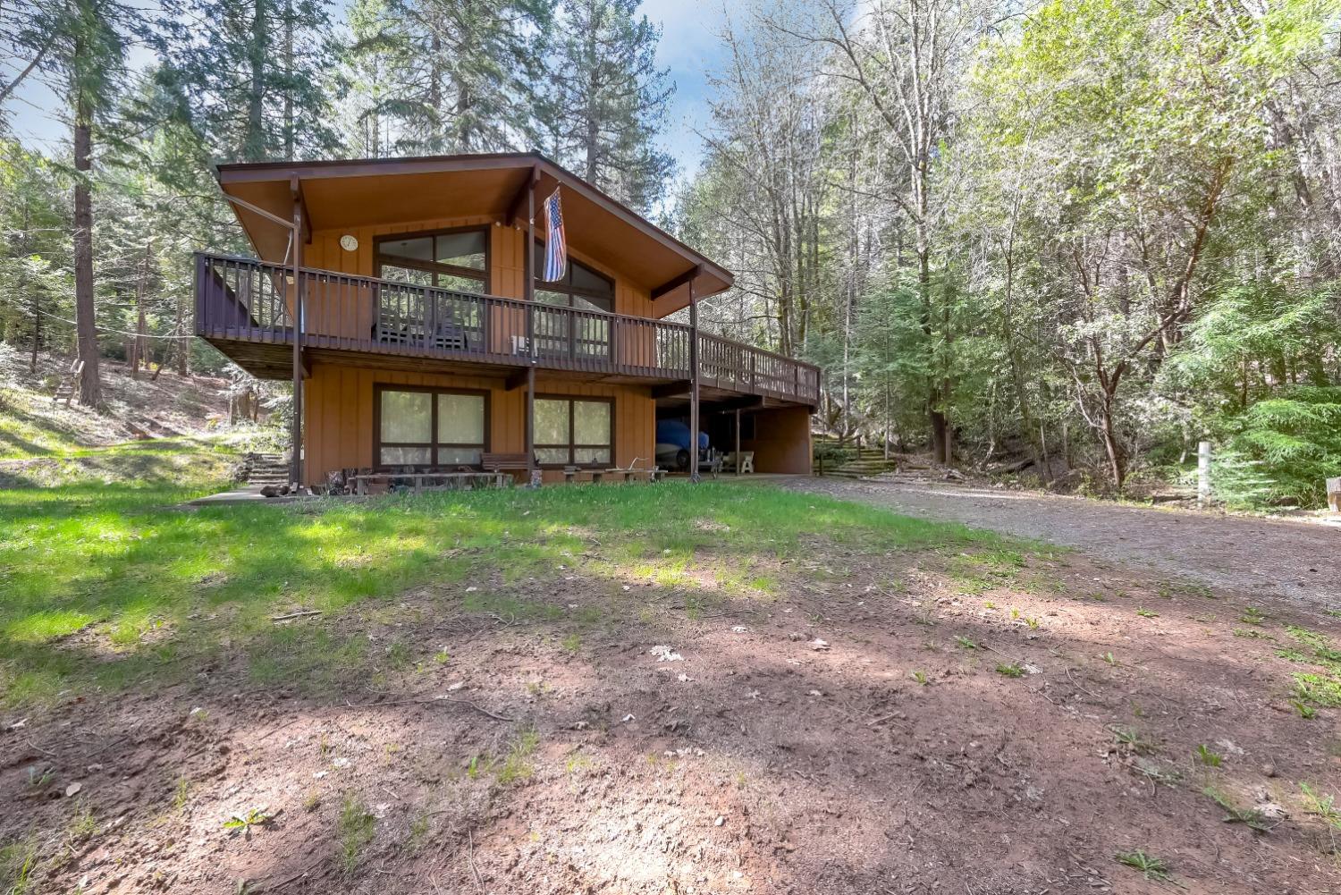 Wooded two-story home with a wide elevated deck and covered parking area beneath it.