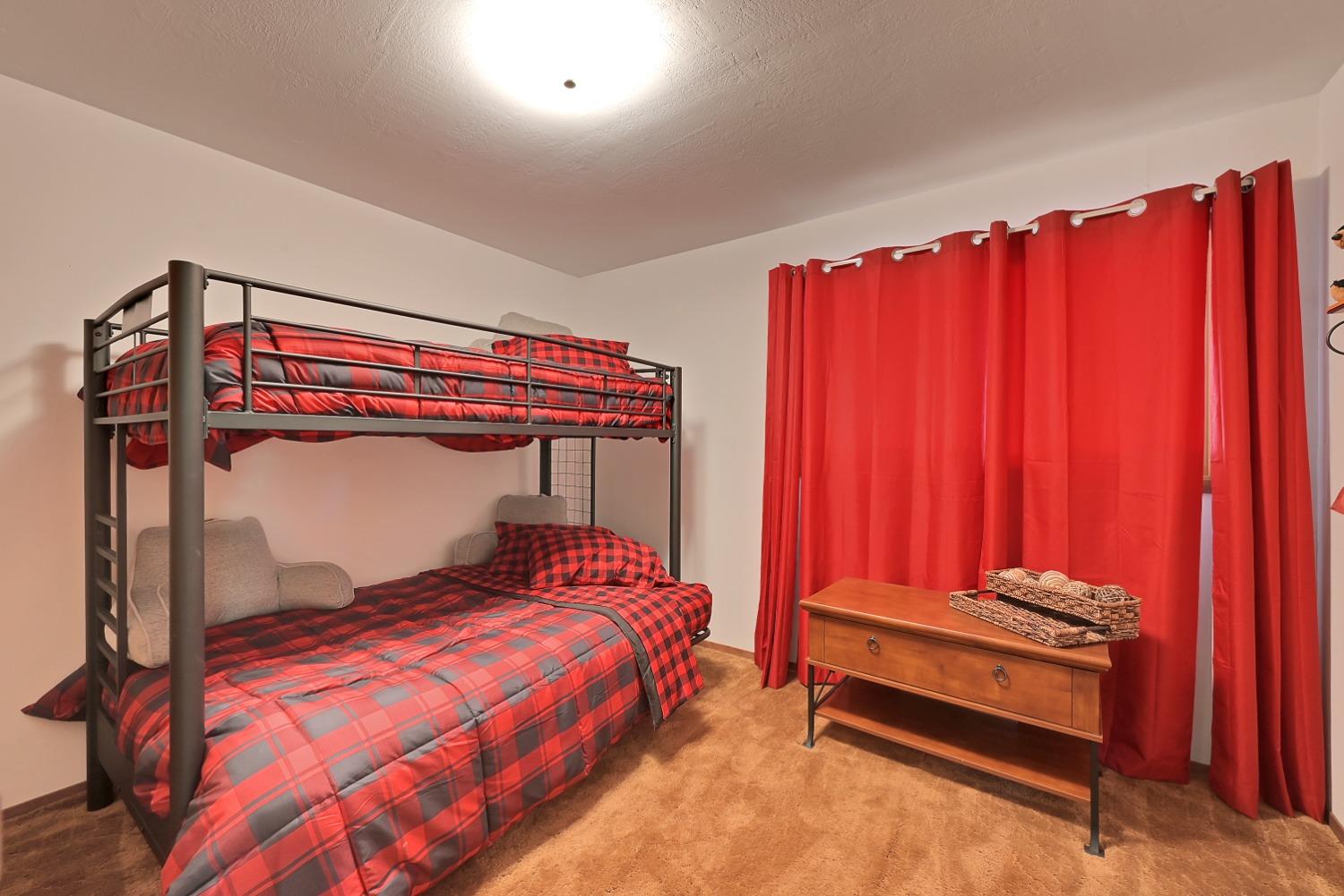 Bedroom with a black metal bunk bed, red plaid bedding, and bright red curtains.