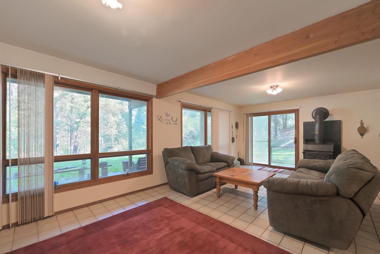 Living room with gray sofas, a wood stove, and large windows overlooking trees.
