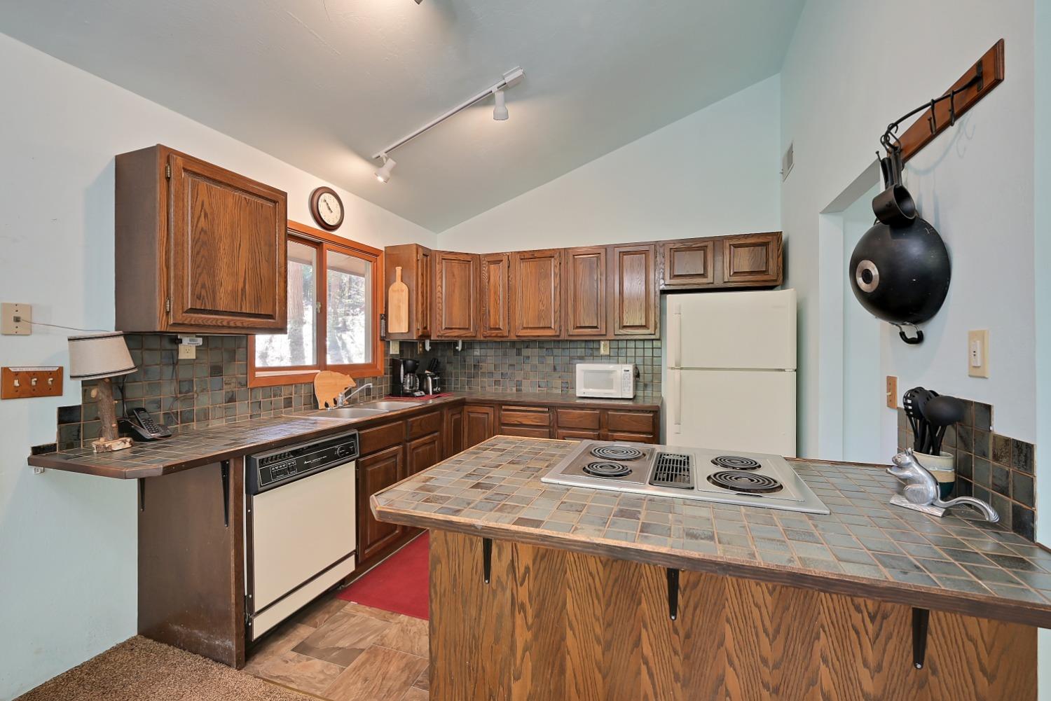 Kitchen with dark wood cabinets, tiled counters, and a large peninsula cooktop.