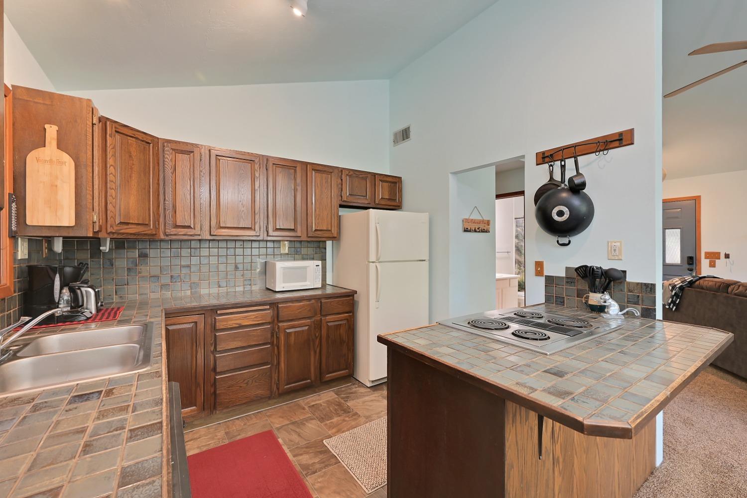 Kitchen with dark wood cabinets, tiled counters, and a large island with an electric cooktop.