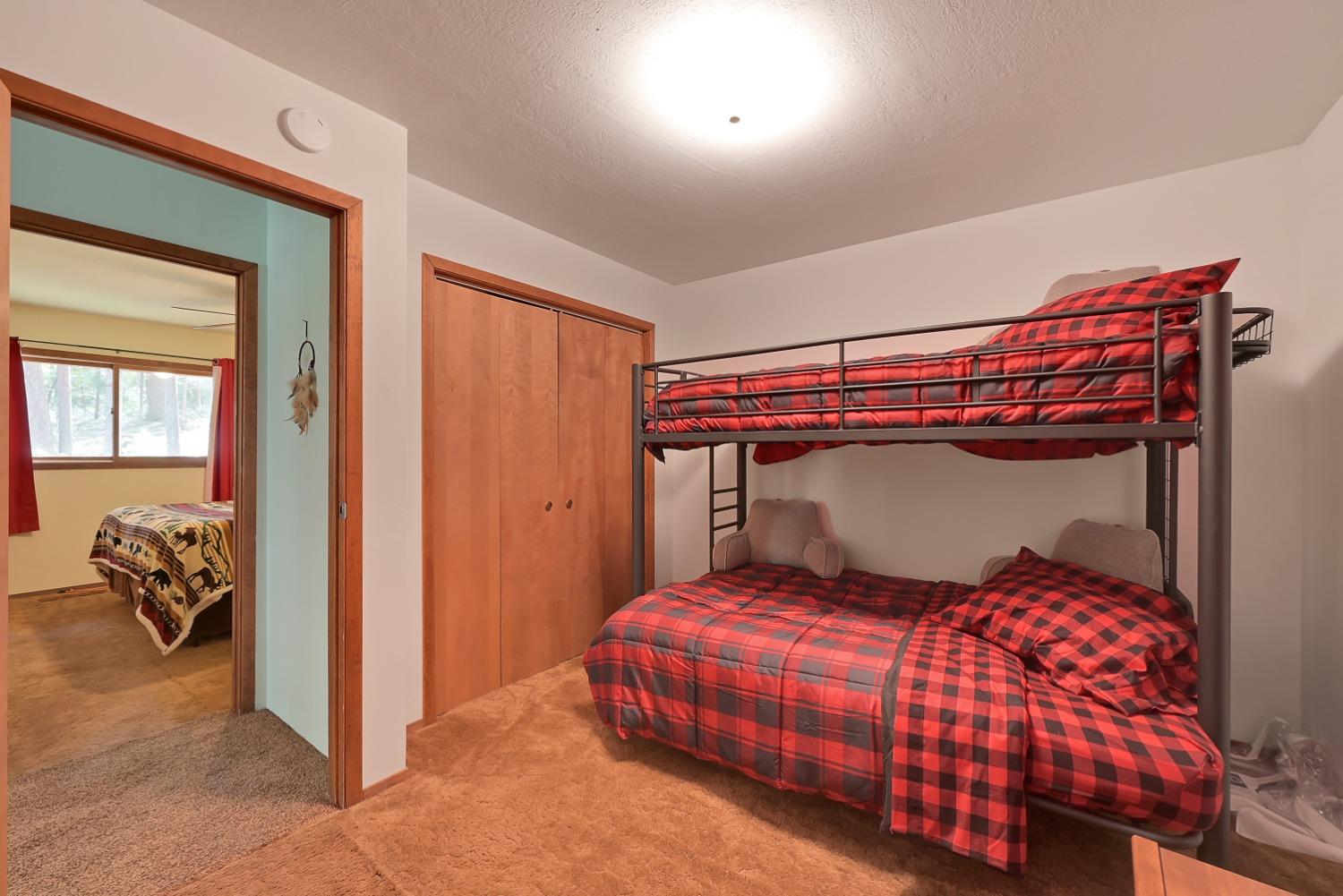 Bedroom with a red-and-black plaid bunk bed and wooden closet, looking through a doorway into another bedroom.