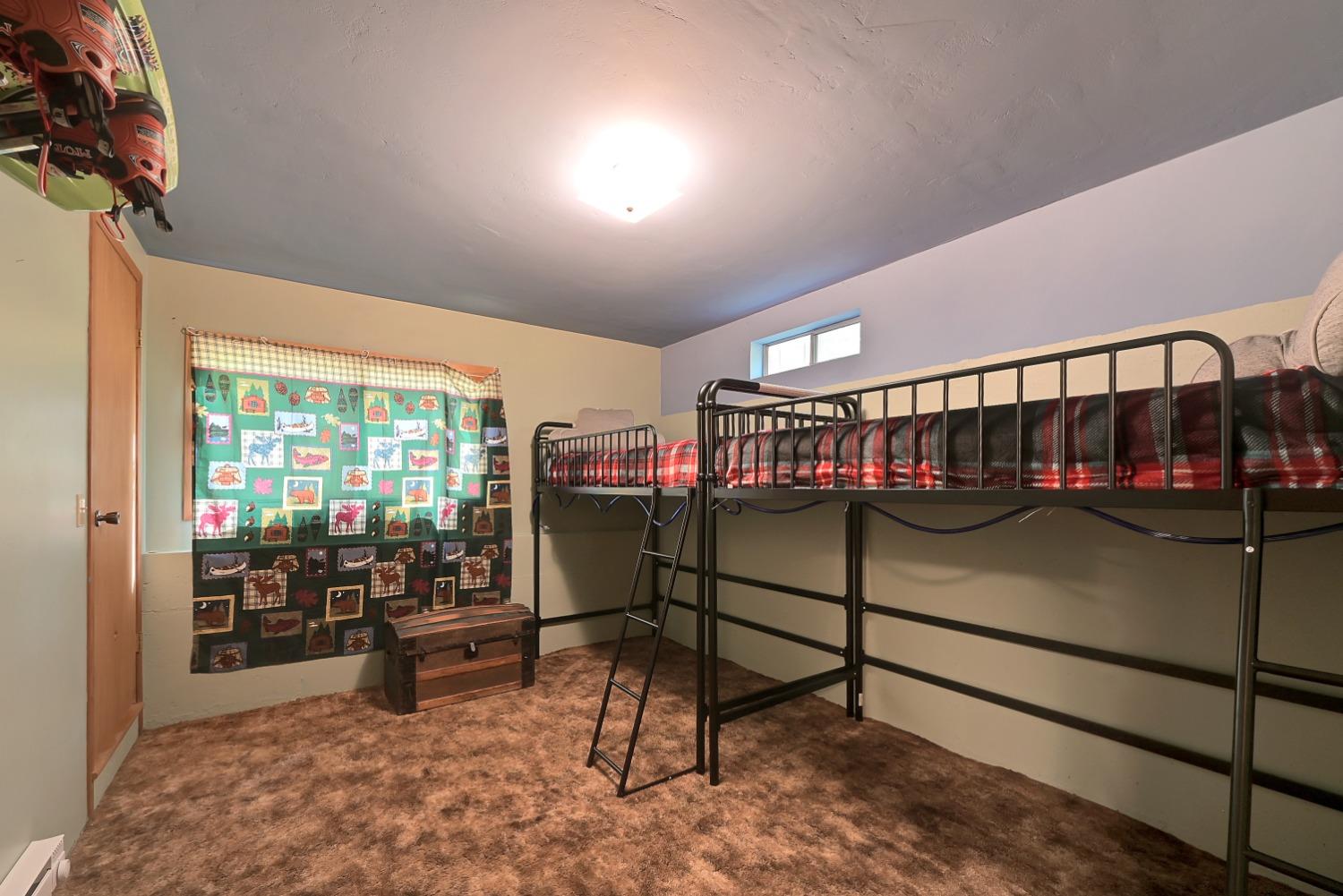 Bedroom with black metal bunk beds, red plaid bedding, and a colorful animal-print curtain.
