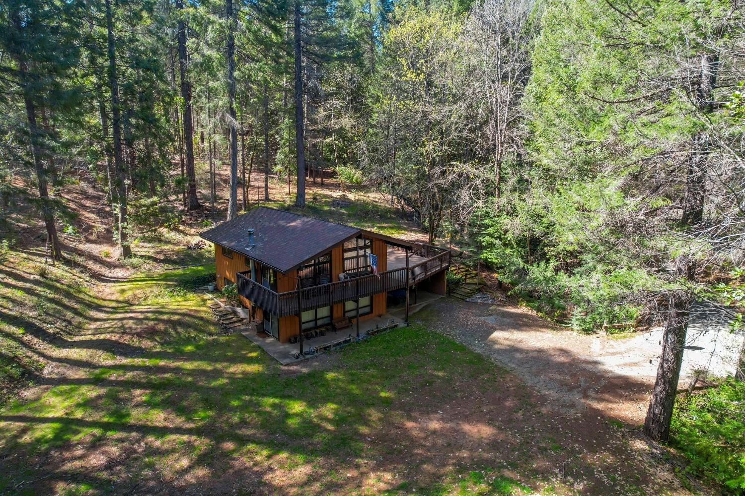 Aerial view of a wood-sided home with a broad deck set among dense trees.