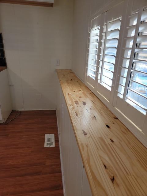 Kitchen with a long light-wood counter beneath tall white plantation shutters.