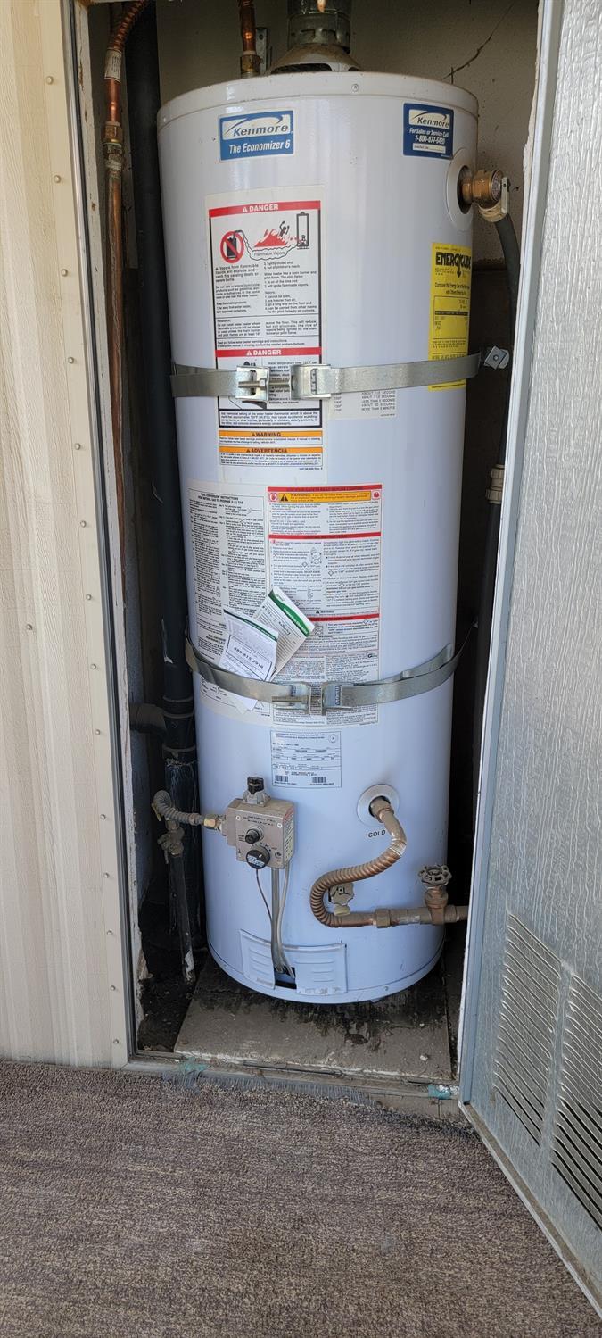 Kenmore gas water heater secured with metal straps in a utility closet.