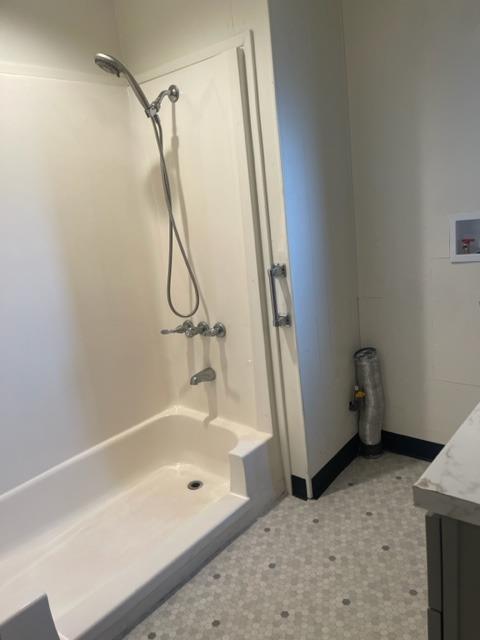 Bathroom with a white shower-tub enclosure, handheld showerhead, and patterned tile floor.