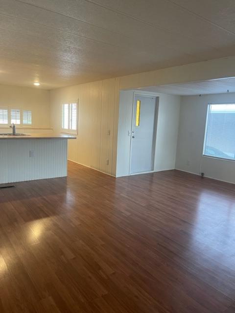 Empty living room with glossy wood-look floors, a front door, and a large window with blinds.