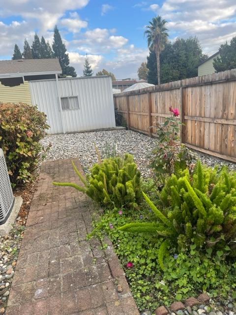 Backyard with a brick-paver walkway, dense shrubs, gravel area, and wooden privacy fence.