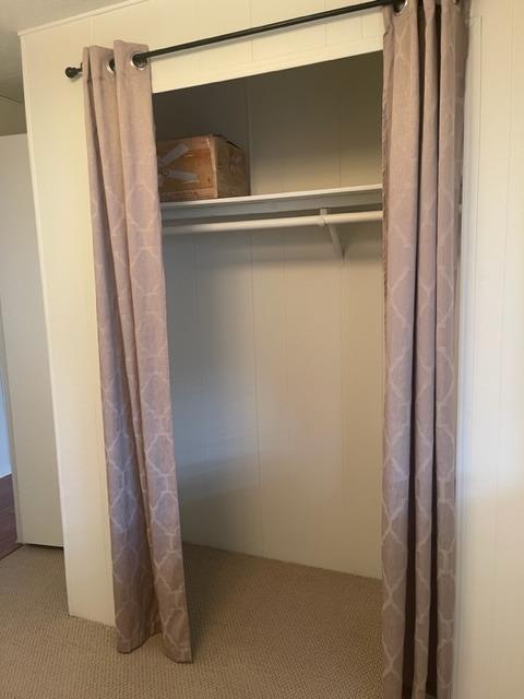 Open closet with mauve curtains, an upper shelf, and beige carpet.