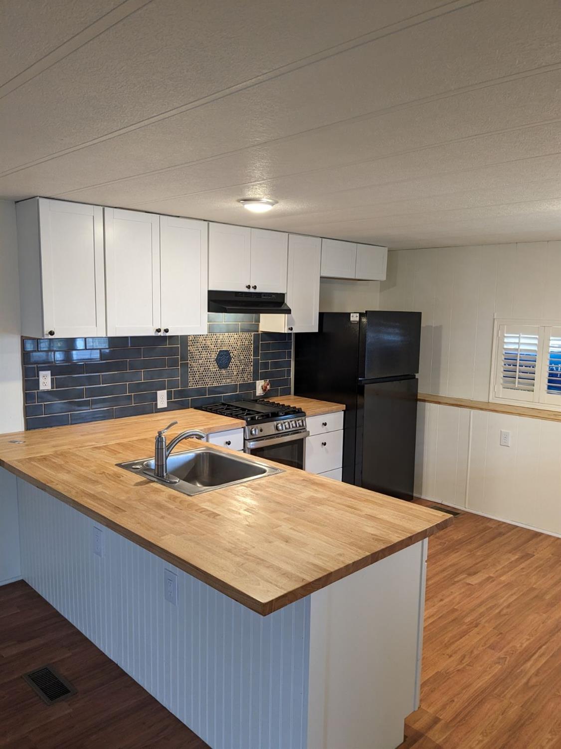 Kitchen with butcher-block counters, a blue tile backsplash, white cabinets, and a large sink peninsula.