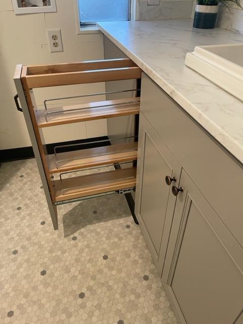Kitchen with an extended wooden pull-out cabinet rack, white cabinets, and hexagonal mosaic flooring.