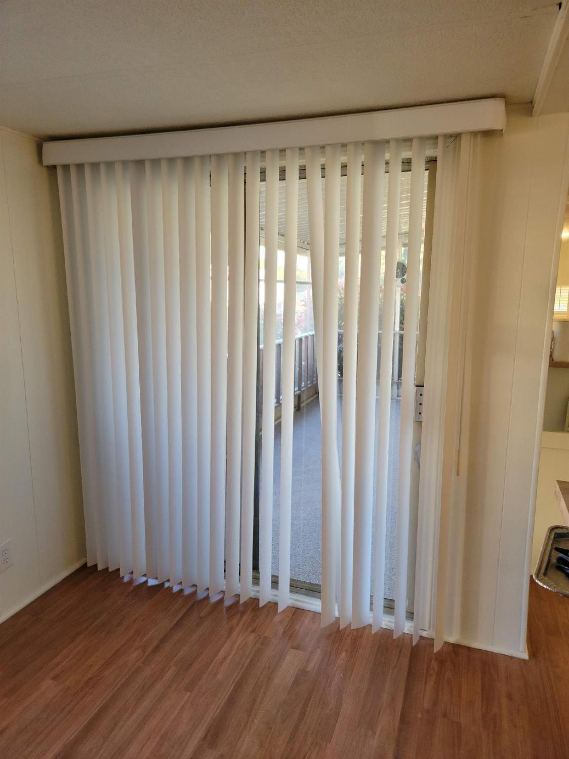 Room with wood-look flooring and white vertical blinds over a sliding glass door opening to a patio.