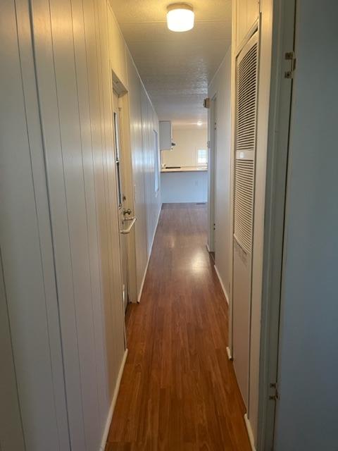 Narrow hallway with reddish wood-look flooring, paneled walls, and a louvered closet door.