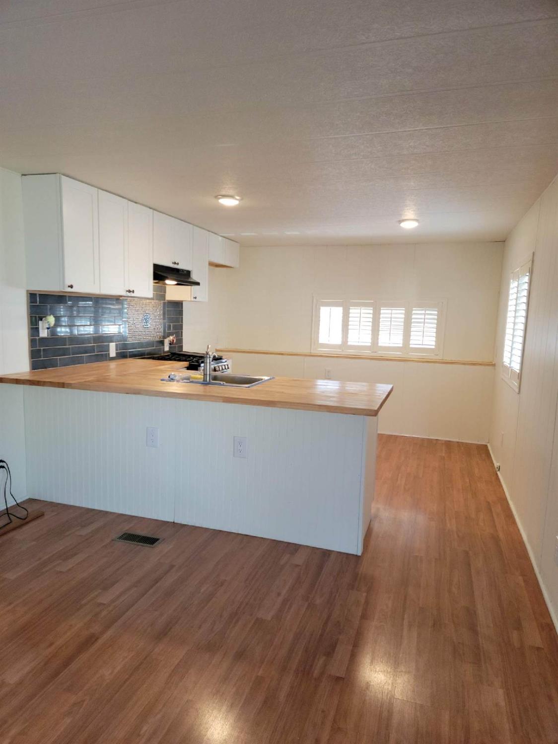 Kitchen with white cabinets, dark blue tile backsplash, and a wood-topped peninsula with sink.