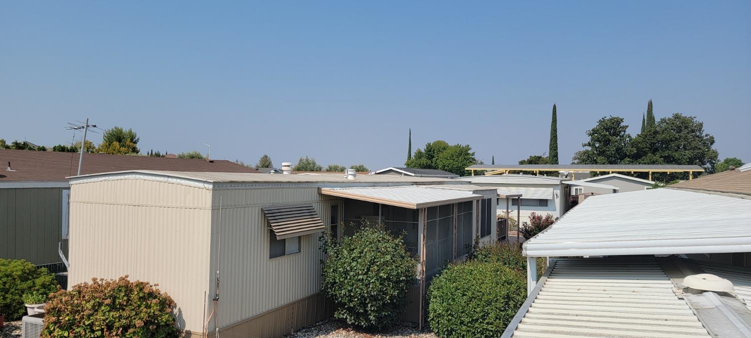 Beige manufactured home with a covered screened patio and shrubs, surrounded by neighboring homes.