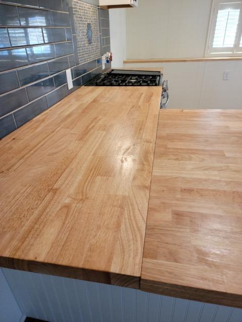 Kitchen with butcher-block countertops, a gas cooktop, and dark tile backsplash.
