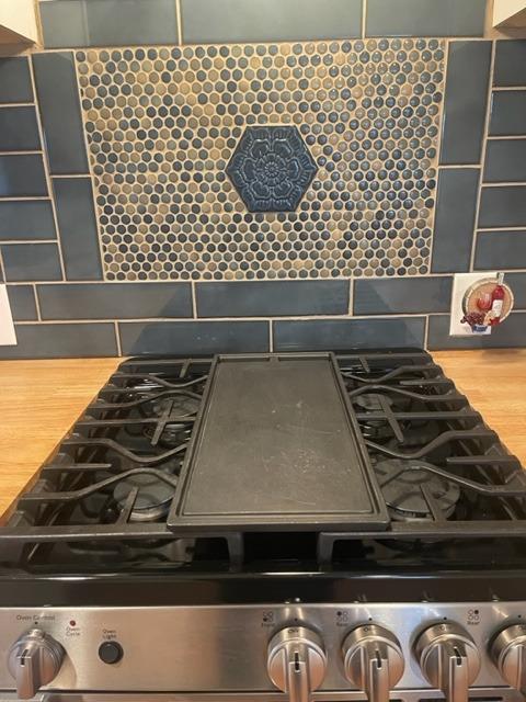 Gas range with central griddle beneath a patterned circular-tile backsplash.
