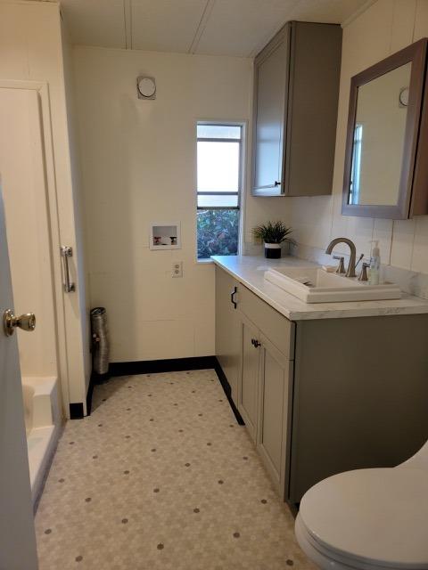 Bathroom with a white vanity, mirrored medicine cabinet, toilet, and small window.