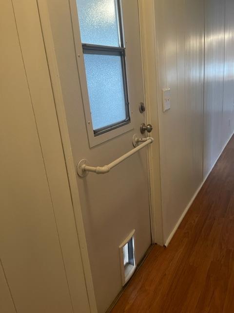 Hallway with a frosted-window door, grab bar, pet door, and reddish-brown wood flooring.