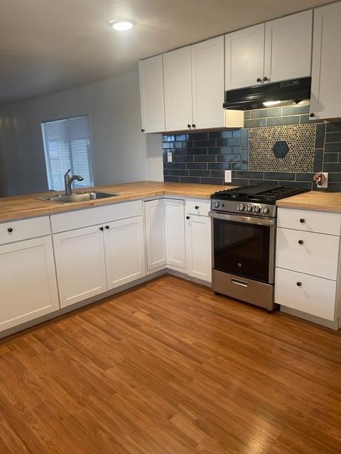 Kitchen with white cabinets, wood countertops, and a dark blue tile backsplash behind the range.