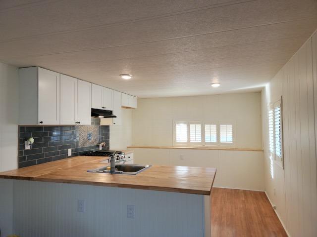 Vacant kitchen with a wood-countertop peninsula, dark tile backsplash, and white cabinets.