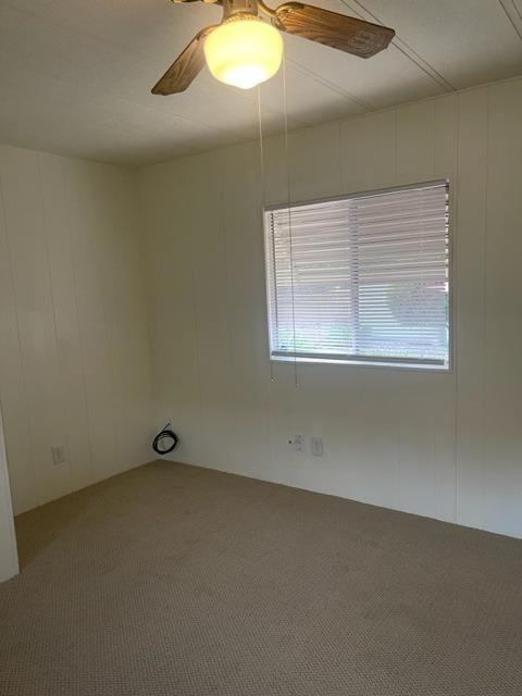 Empty carpeted bedroom with a window, horizontal blinds, and a wood ceiling fan.