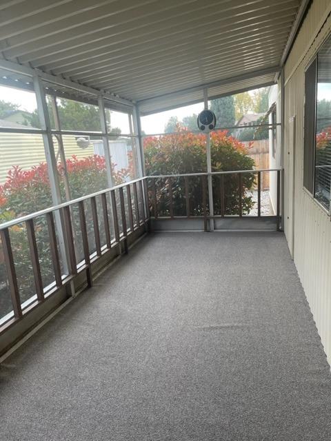 Screened-in porch with gray flooring, metal railings, and red-leaved shrubs outside.