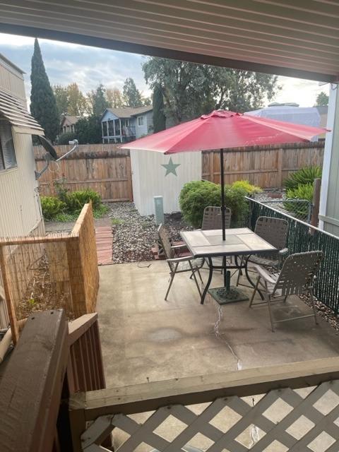 Covered backyard patio with outdoor dining set, red umbrella, wooden fence, and gravel landscaping.