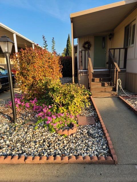 Home entrance with a covered porch, green door, wooden steps, and a flower-filled rock garden.